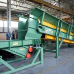 Apron conveyor industriale Ghirarduzzi con struttura inclinata e piastre metalliche, progettato per il trasporto continuo di materiali pesanti in fonderia o impianti di riciclo. Ideale per il carico dei forni o l’alimentazione di mulini.