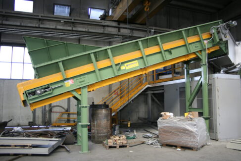 Trasportatore Apron Conveyor inclinato Ghirarduzzi con piastre metalliche robuste per carico forni, alimentazione mulini e applicazioni nel riciclaggio, realizzato su struttura industriale ad alta resistenza.
