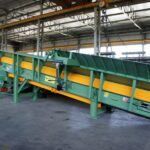 Trasportatore Apron conveyor inclinato realizzato da Ghirarduzzi, dotato di piastre metalliche resistenti e struttura modulare. Ideale per il trasporto di materiali pesanti in fonderia, per il carico dei forni o l’alimentazione dei mulini, impiegato anche nel settore del riciclaggio industriale.
