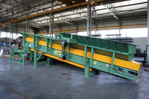 Trasportatore Apron conveyor inclinato realizzato da Ghirarduzzi, dotato di piastre metalliche resistenti e struttura modulare. Ideale per il trasporto di materiali pesanti in fonderia, per il carico dei forni o l’alimentazione dei mulini, impiegato anche nel settore del riciclaggio industriale.