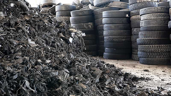 Ammasso di frammenti di pneumatici riciclati con pile di gomme intere sullo sfondo, evidenziando il processo di riciclo e riutilizzo dei materiali.